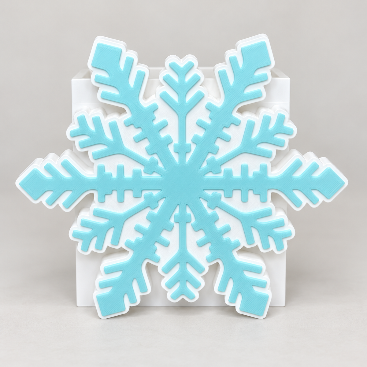 White and light turquoise snowflake cover displayed on an empty white interchangeable base. Base sold separately. Enhanced product photo.