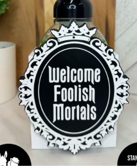 Black and white ornate oval cover with a crown and the words Welcome Foolish Mortals. Base and soap bottle not included.